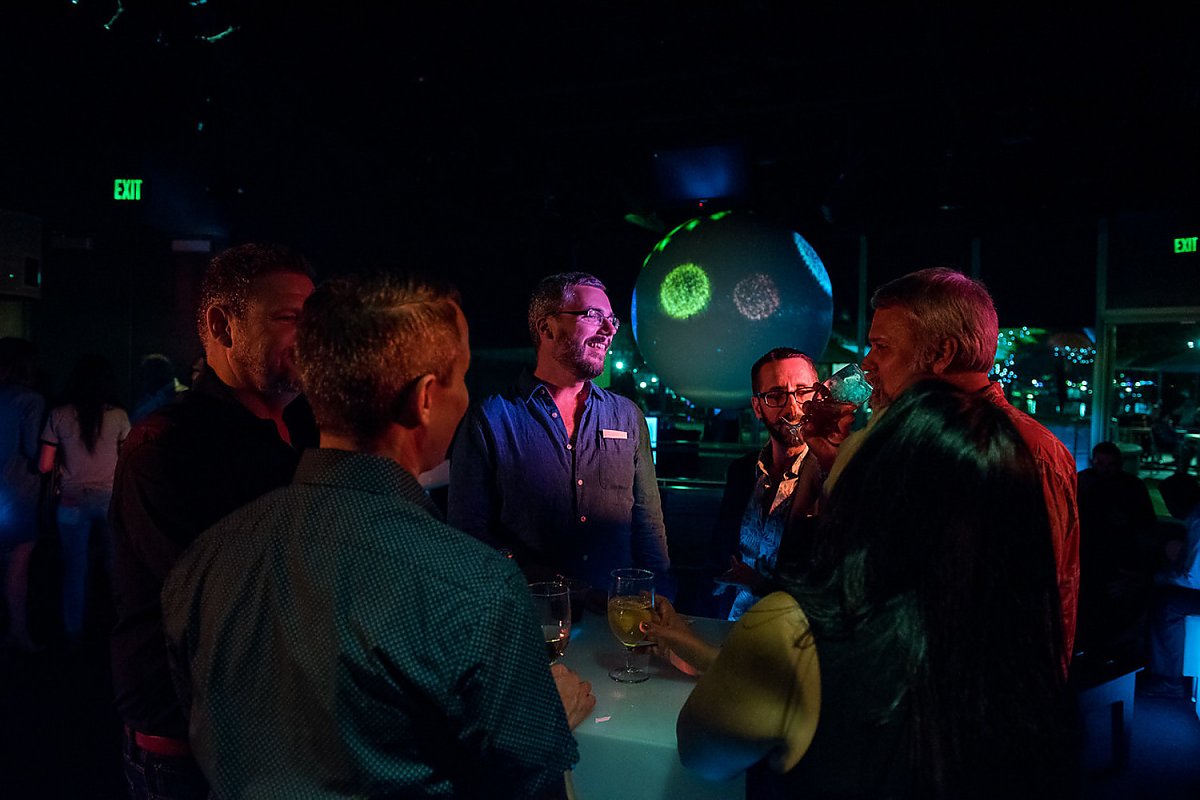 Group of people engaged in conversation at a social gathering, with a large illuminated globe in the background.