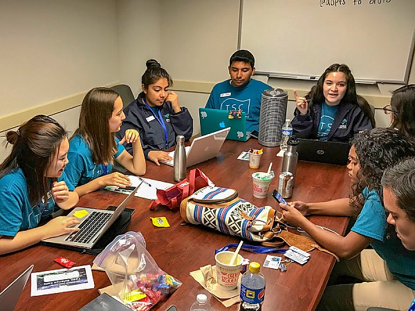 Students gather around a conference table with computers and notebooks